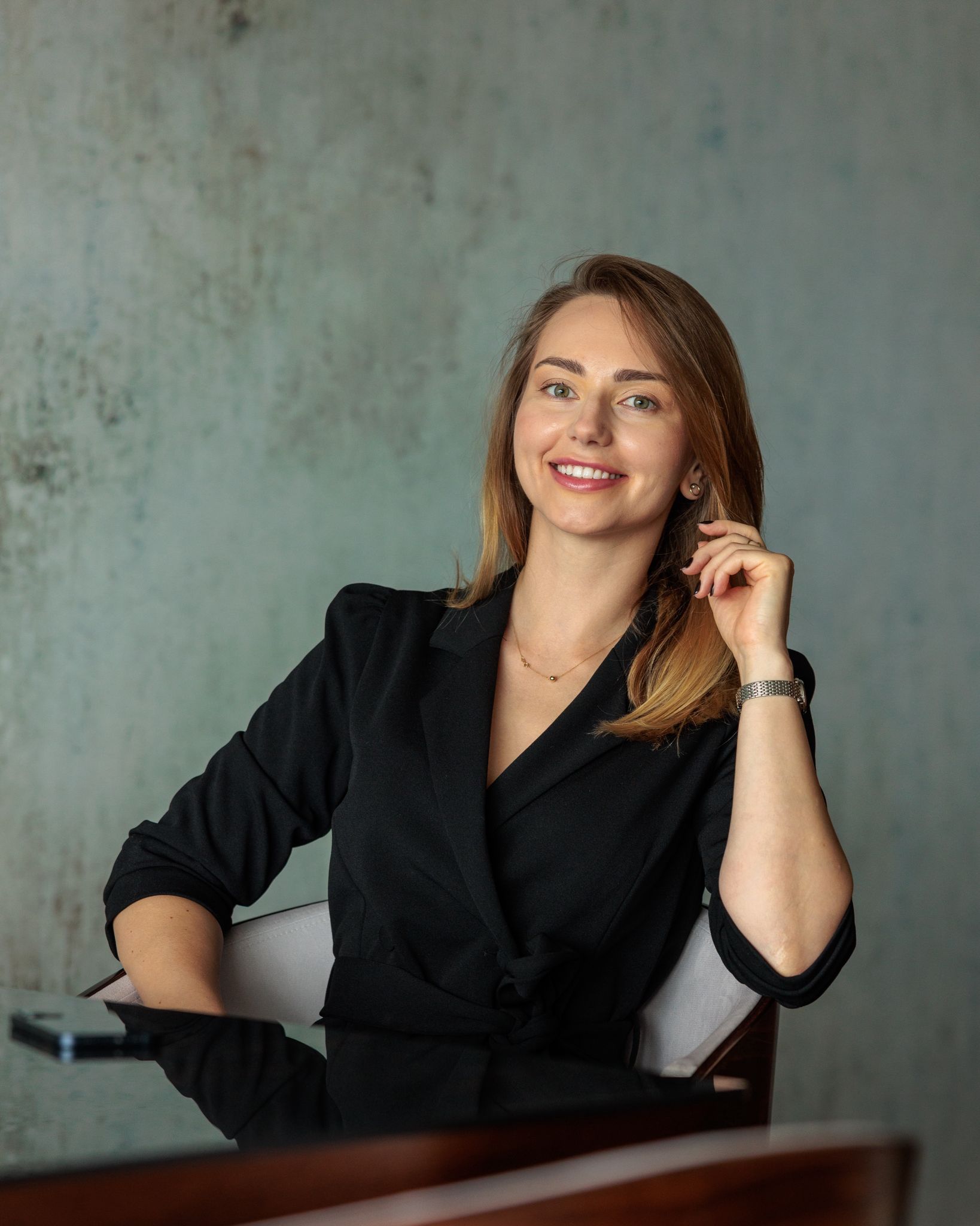 Anastasia Goluk siedzi w fotelu w czarnej marynarce i uśmiecha się szeroko